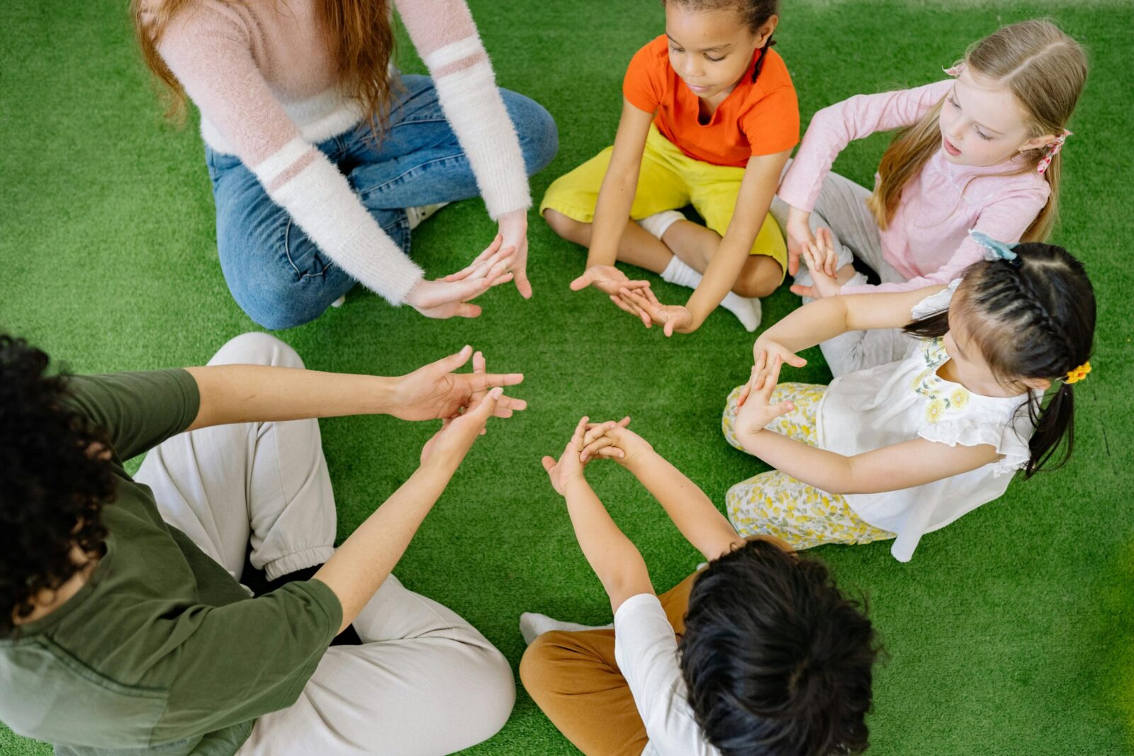 Children sitting in a circle playing fun team games on artificial grass.